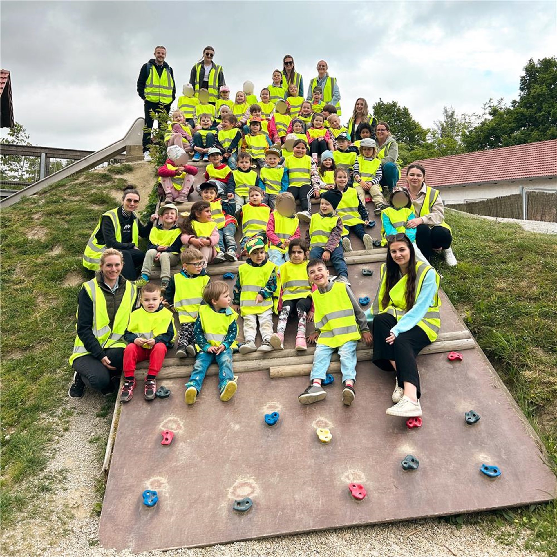 Eine Kindergartengruppe trägt gelbe Westen und sitzt auf einer Kletterrampe auf einem Spielplatz.
